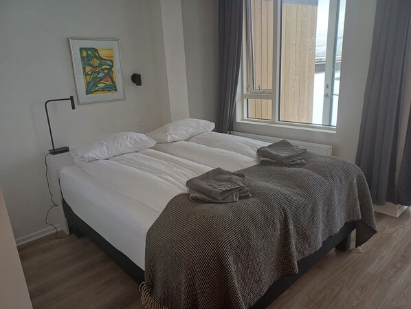A neatly made bed with white linens and a patterned blanket, a bedside lamp, and a framed abstract painting on the wall.