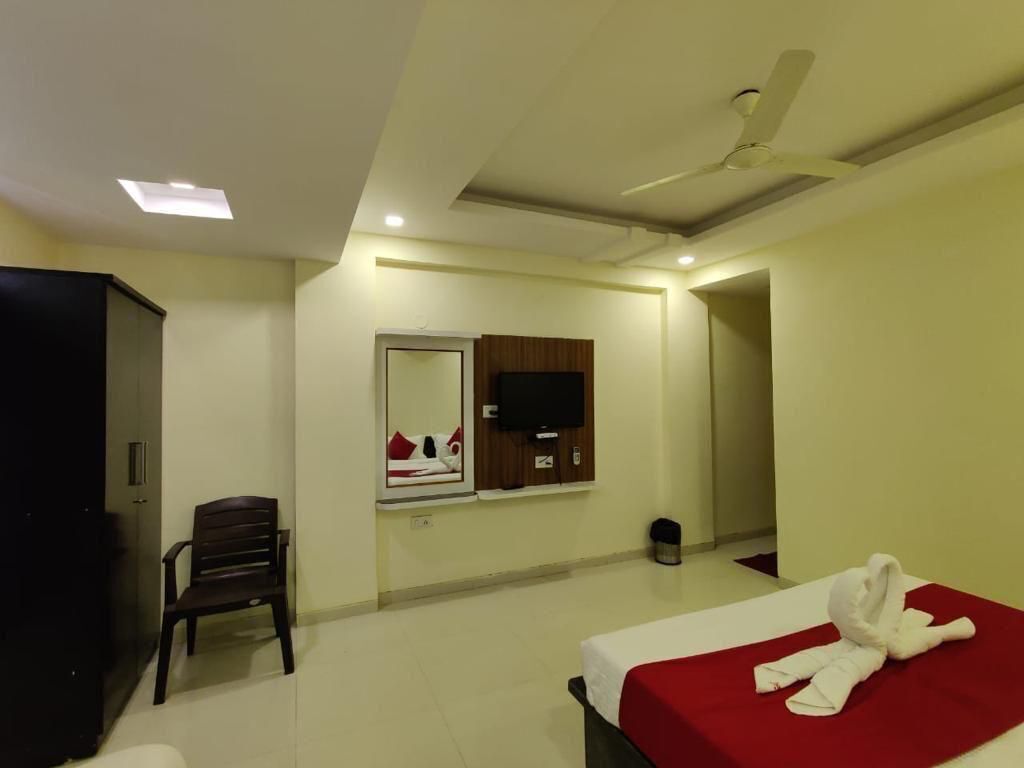 Una habitación de hotel con cama, sillón, televisión y ventilador de techo.