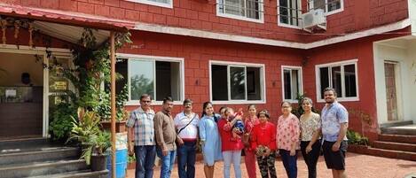 A group of people standing in front of a red brick building with multiple windows and air conditioning units.