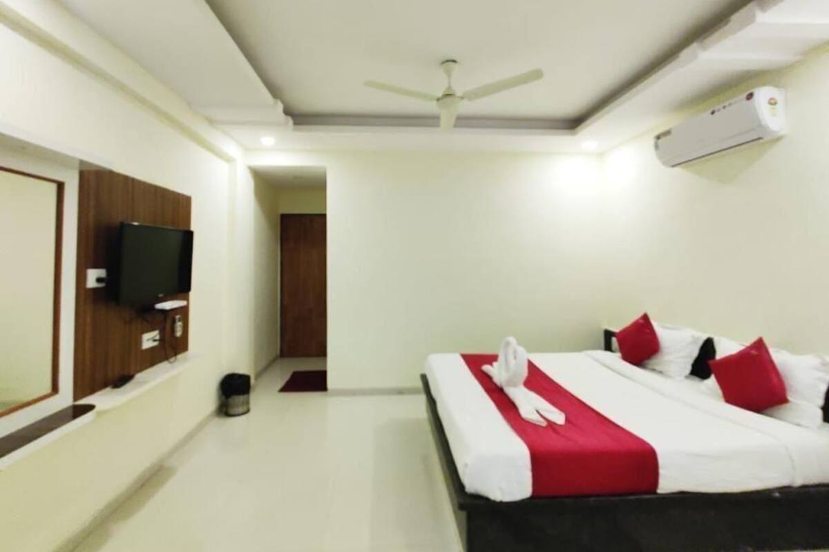 A hotel room with a bed, a ceiling fan, a TV, and an air conditioning unit.
