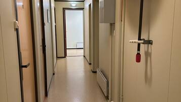 A hotel corridor with doors on both sides, a fire alarm sign, and a red fire hose reel on the right wall.