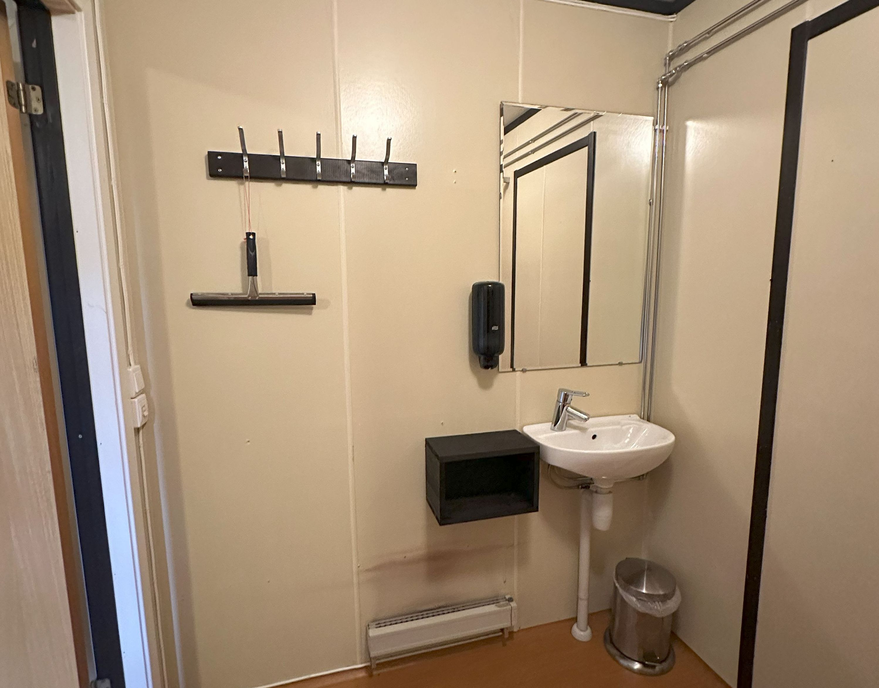 Un baño con un lavamanos blanco, un espejo, dispensador de jabón, toallero y un cubo de basura.