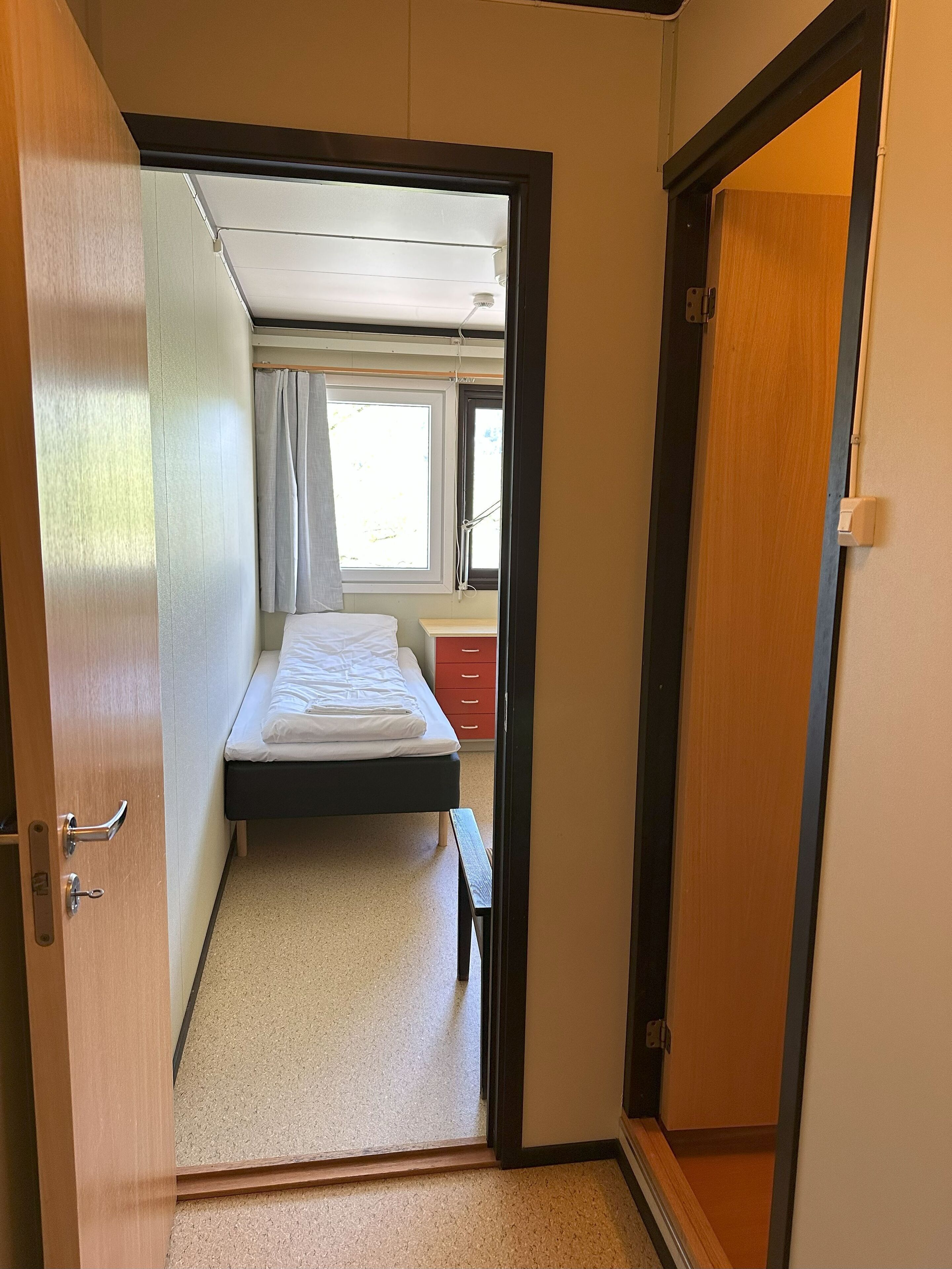 Un dormitorio pequeño con cama individual, una mesita de noche y una ventana con cortinas.