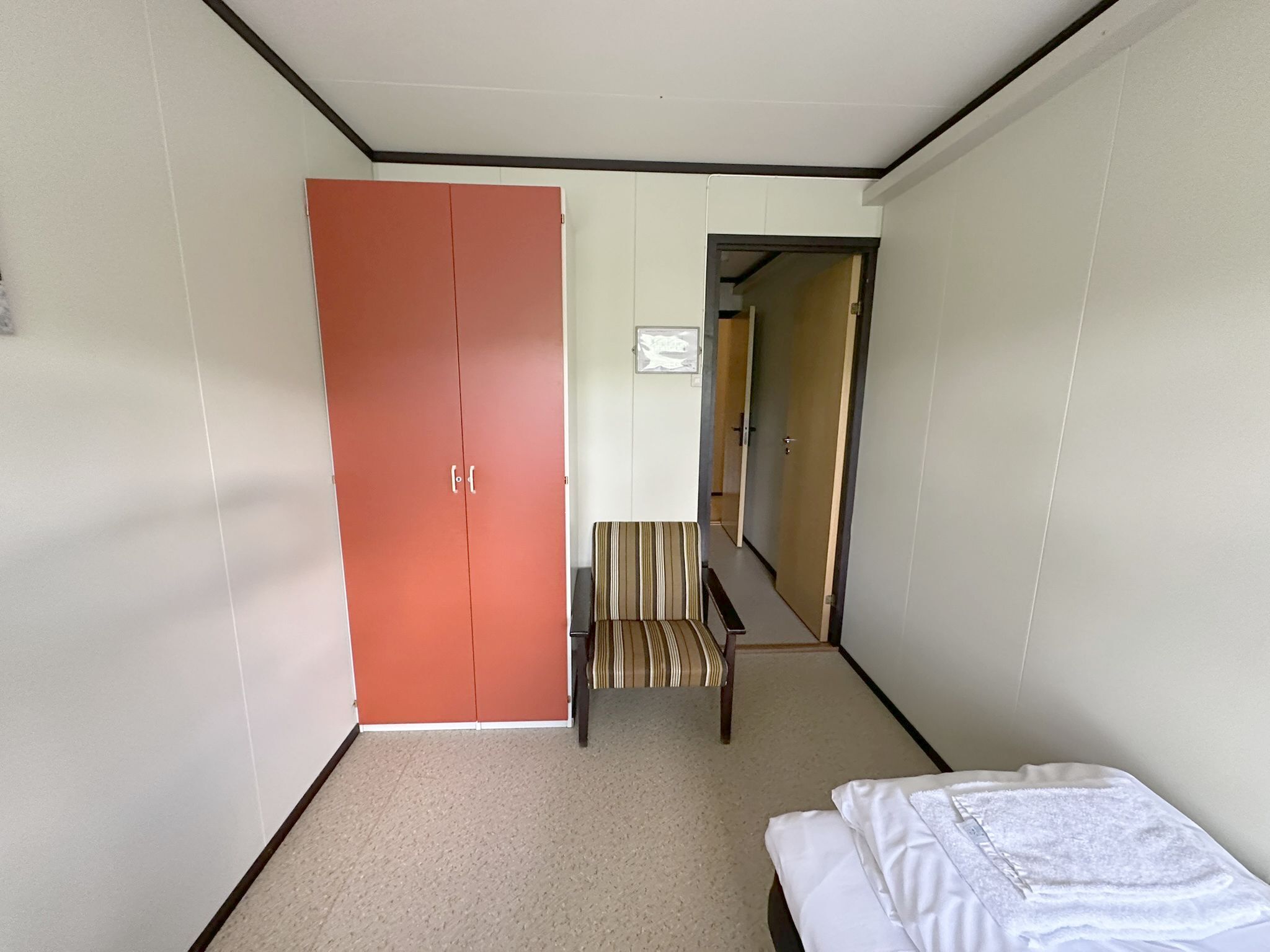 Une chambre d’hôtel avec un lit, un banc, une chaise à rayures et une armoire.