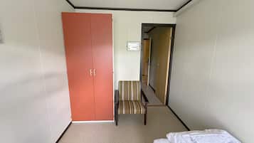 Une chambre d’hôtel avec un lit, un banc, une chaise à rayures et une armoire.