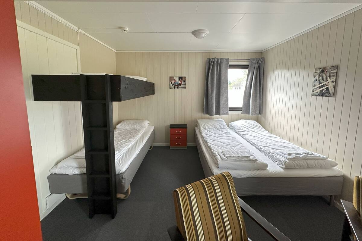 Habitación tipo dormitorio con literas, un escritorio pequeño, una silla y una ventana con cortinas.