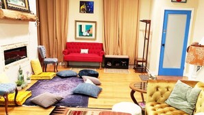 A cozy living room with a red sofa, yellow sofa, and a wooden coffee table. There is a fireplace, a blue door, and a red wall decoration. - MASSiVE Bohemian Oasis in Philly 5 BdrmSleeps 12 (Philadelphia)