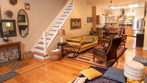 A spacious living area with a staircase, a sofa, a coffee table, and a dining area with chairs and a chandelier. - MASSiVE Bohemian Oasis in Philly 5 BdrmSleeps 12 (Philadelphia)