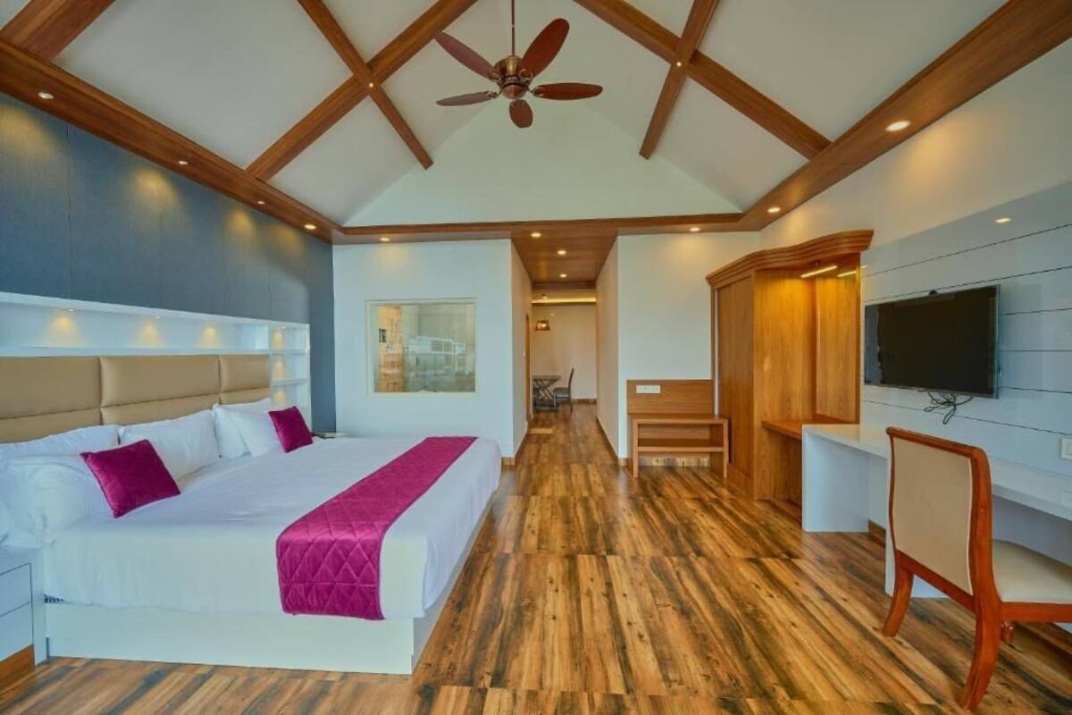 Une chambre d’hôtel moderne avec un grand lit, un plancher en bois, un ventilateur de plafond et un téléviseur fixé au mur.