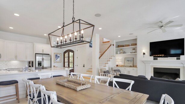 A spacious living area with a wooden dining table, white chairs, a black sofa, and a fireplace. - 7 BR 8 BA Private Pool Singleton Beach Sleeps 24 Bikes & Beach Gear included (Hilton Head Island)