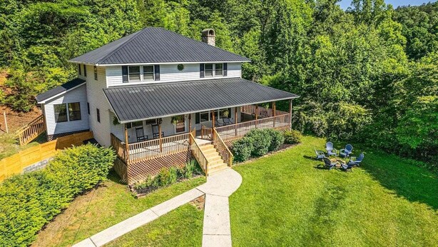 Une maison à deux étages dotée d’un porche et d’une terrasse, entourée d’une pelouse bien entretenue et d’arbres touffus.