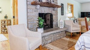 Un salon doté d’une cheminée en pierre, de planchers en bois et de deux fauteuils.