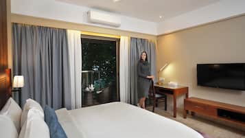 Una habitación de hotel con cama, escritorio, silla, televisor y ventana con cortinas.