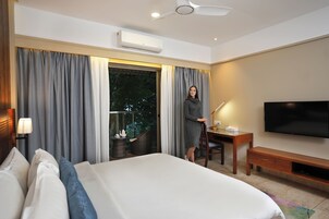 Una habitación de hotel con cama, escritorio, silla, televisor y ventana con cortinas.