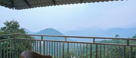 A balcony with wicker chairs, a small table with a teapot and cups, and a view of lush mountains.