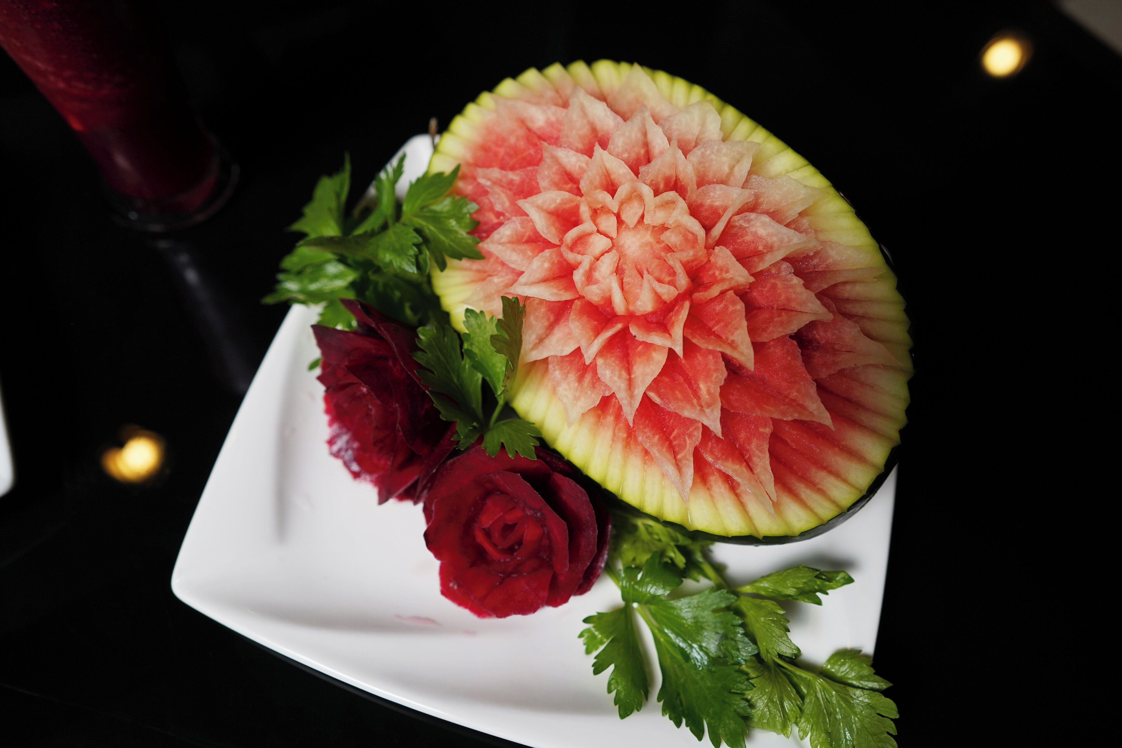 A watermelon carved into a flower with a rose and parsley garnish on a white plate.