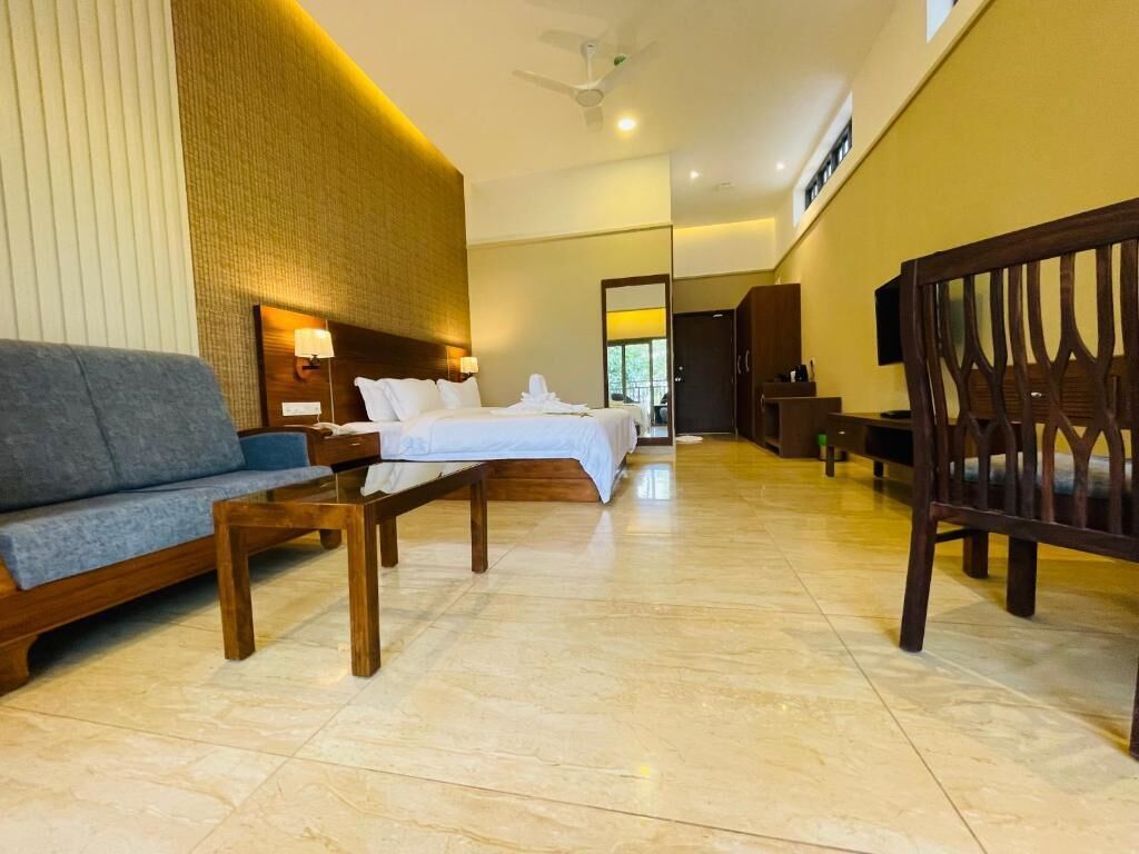 Una habitación de hotel con cama, sofá, una silla de madera y una mesita.