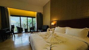 Habitación de hotel con una cama grande, un escritorio y una silla. Tiene un balcón con vista a árboles.