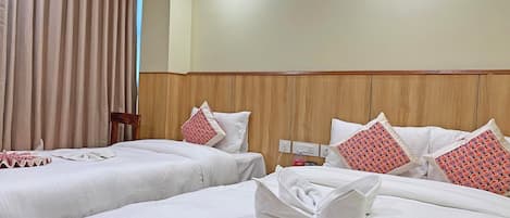 A hotel room with two beds, beige curtains, wooden headboard, white bedding, and patterned pillows.