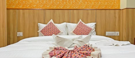 Una cama bien tendida con sábanas blancas y dos almohadones decorativos, un cabecero de madera y una pared con textura.