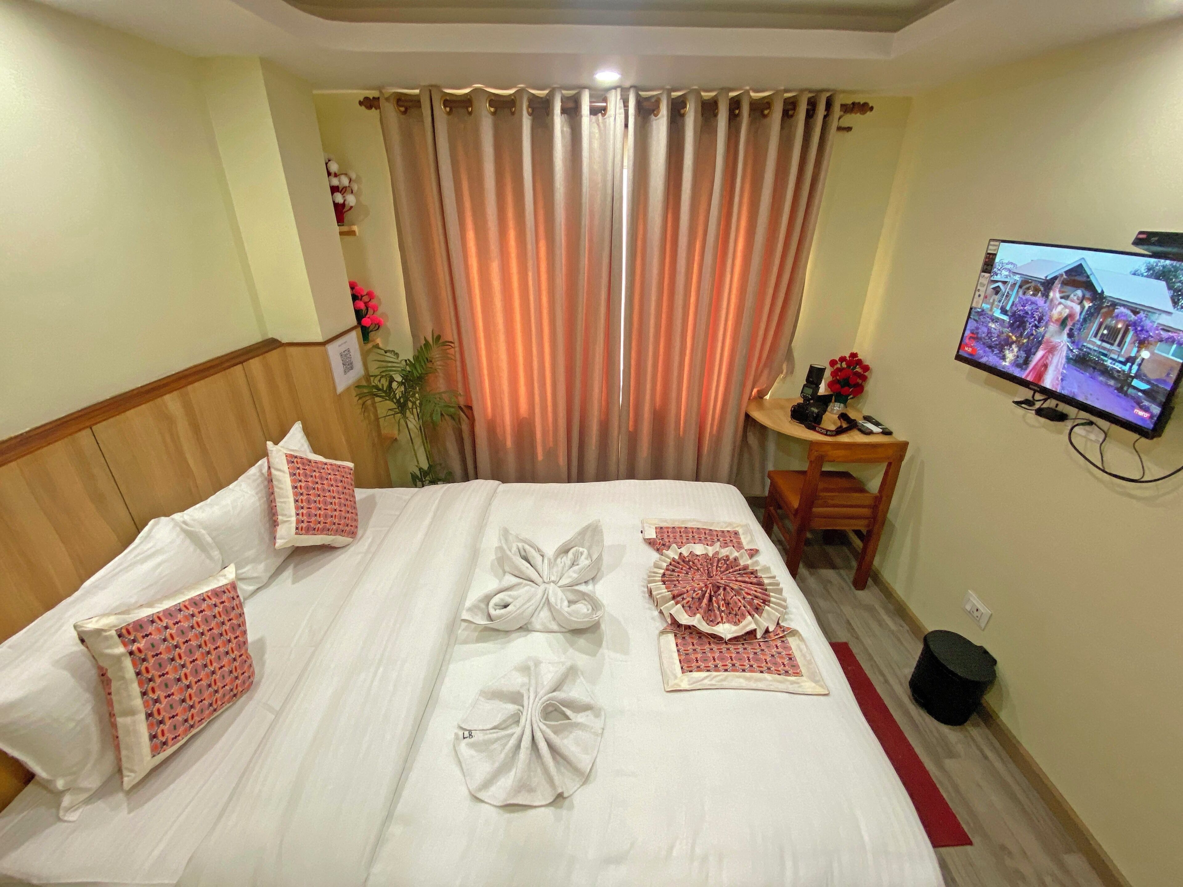 A hotel room with a neatly made bed, a television on the wall, and a small desk with a chair.