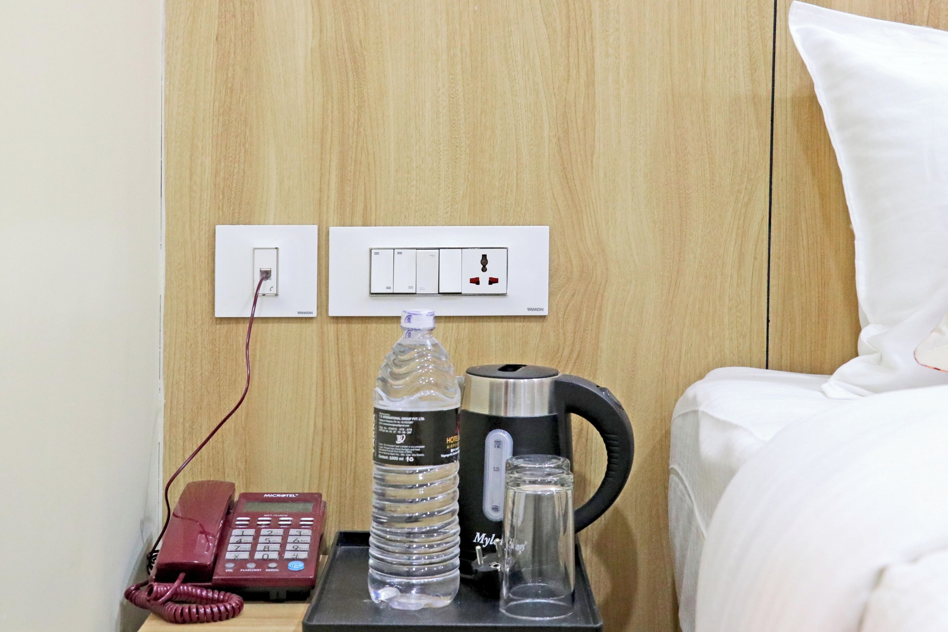 A hotel room with a bed, a bedside table with a telephone, a bottle of water, a glass, and a coffee maker.