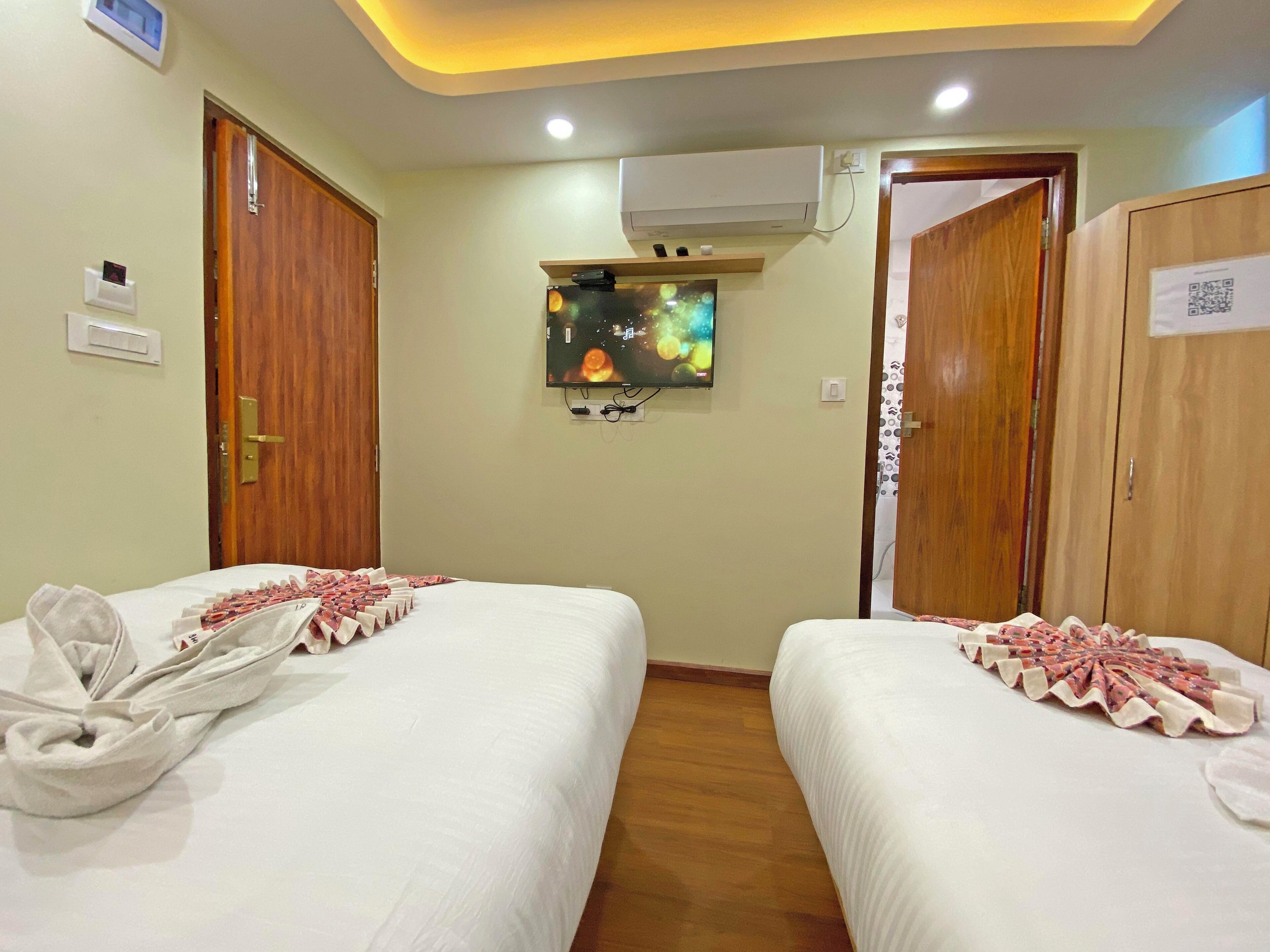 A hotel room with two beds, a TV on the wall, and an air conditioning unit.