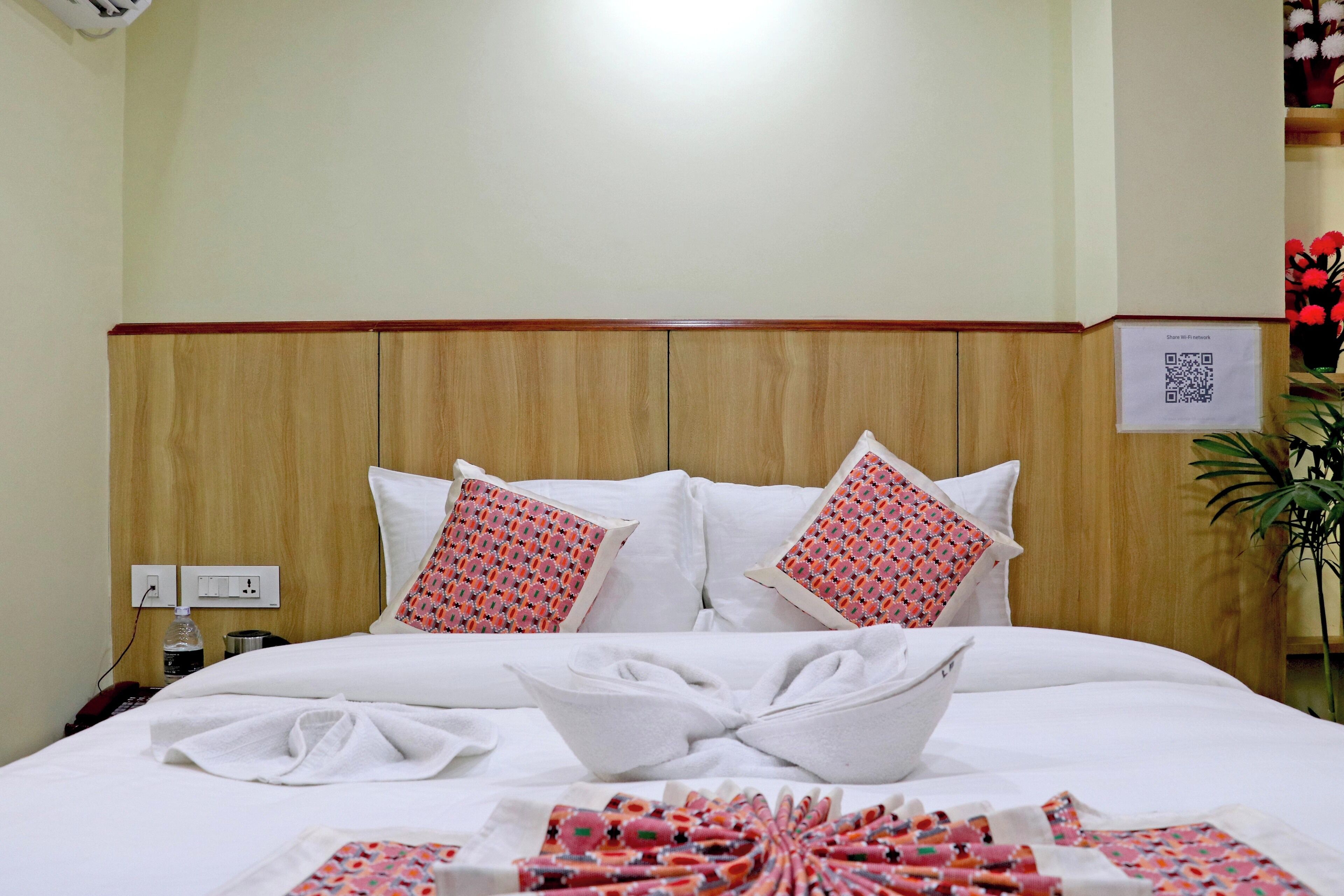 A hotel room with a wooden headboard, white bedding, and two patterned pillows.