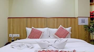 Une chambre d’hôtel avec une tête de lit en bois, du linge de lit blanc et deux coussins à motifs.