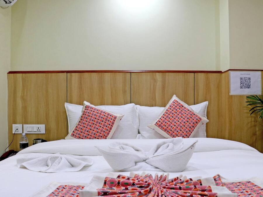 Une chambre d’hôtel avec une tête de lit en bois, du linge de lit blanc et deux coussins à motifs.
