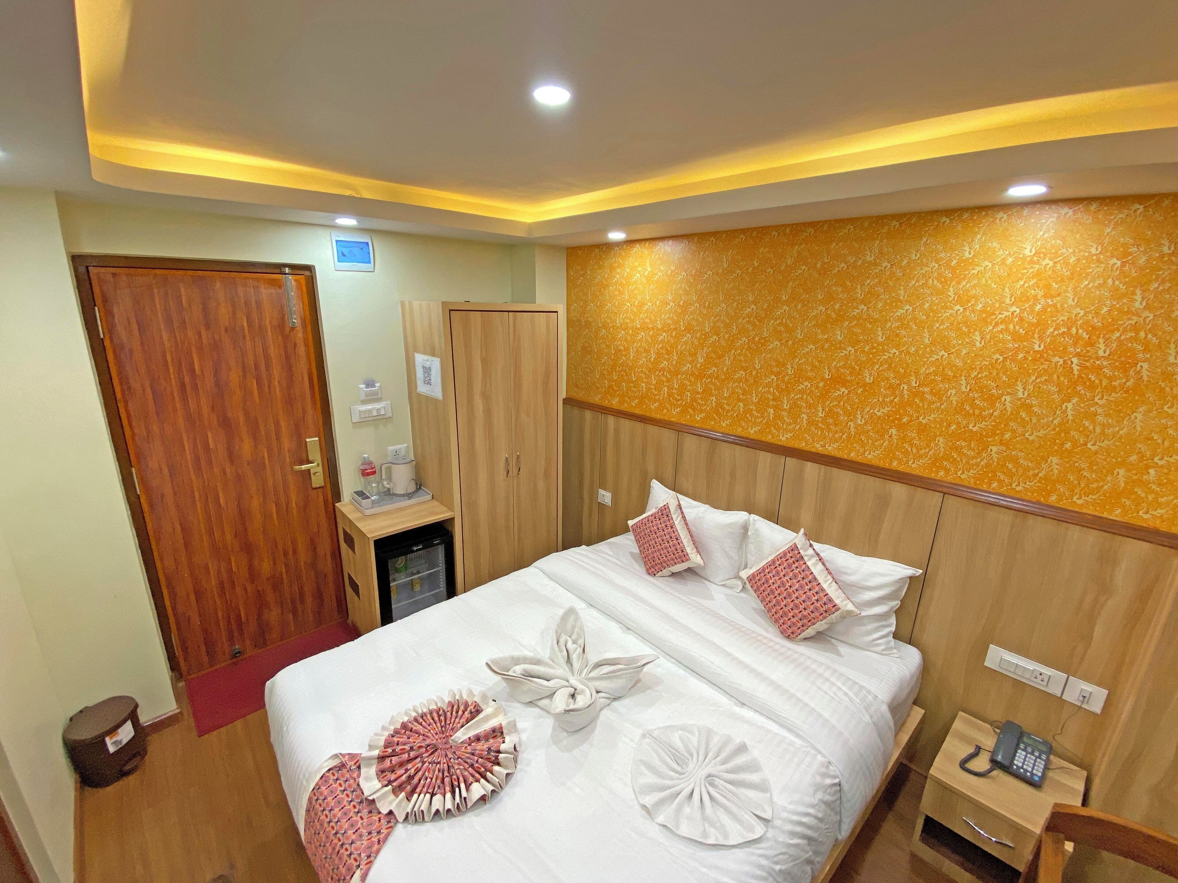 Habitación de hotel con cama, armario, escritorio y teléfono, y pared con diseño decorativo.