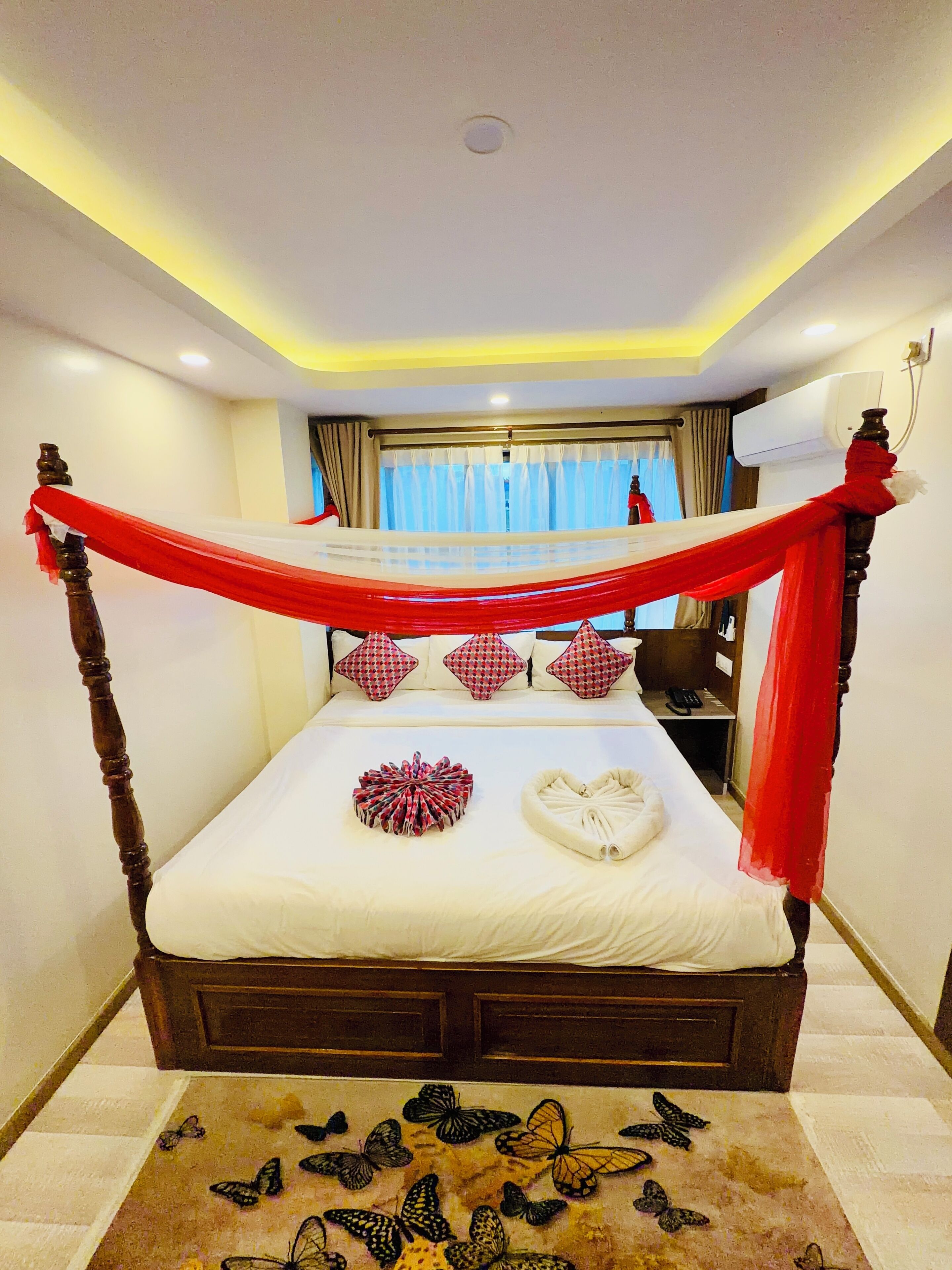 A four-poster bed with a canopy, a bedside table with a lamp, and a window with curtains.