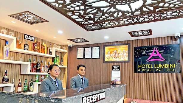 A hotel reception area with a bar, reception desk, and a TV screen displaying a horse race. - Hotel Lumbini Airport (Kathmandu)