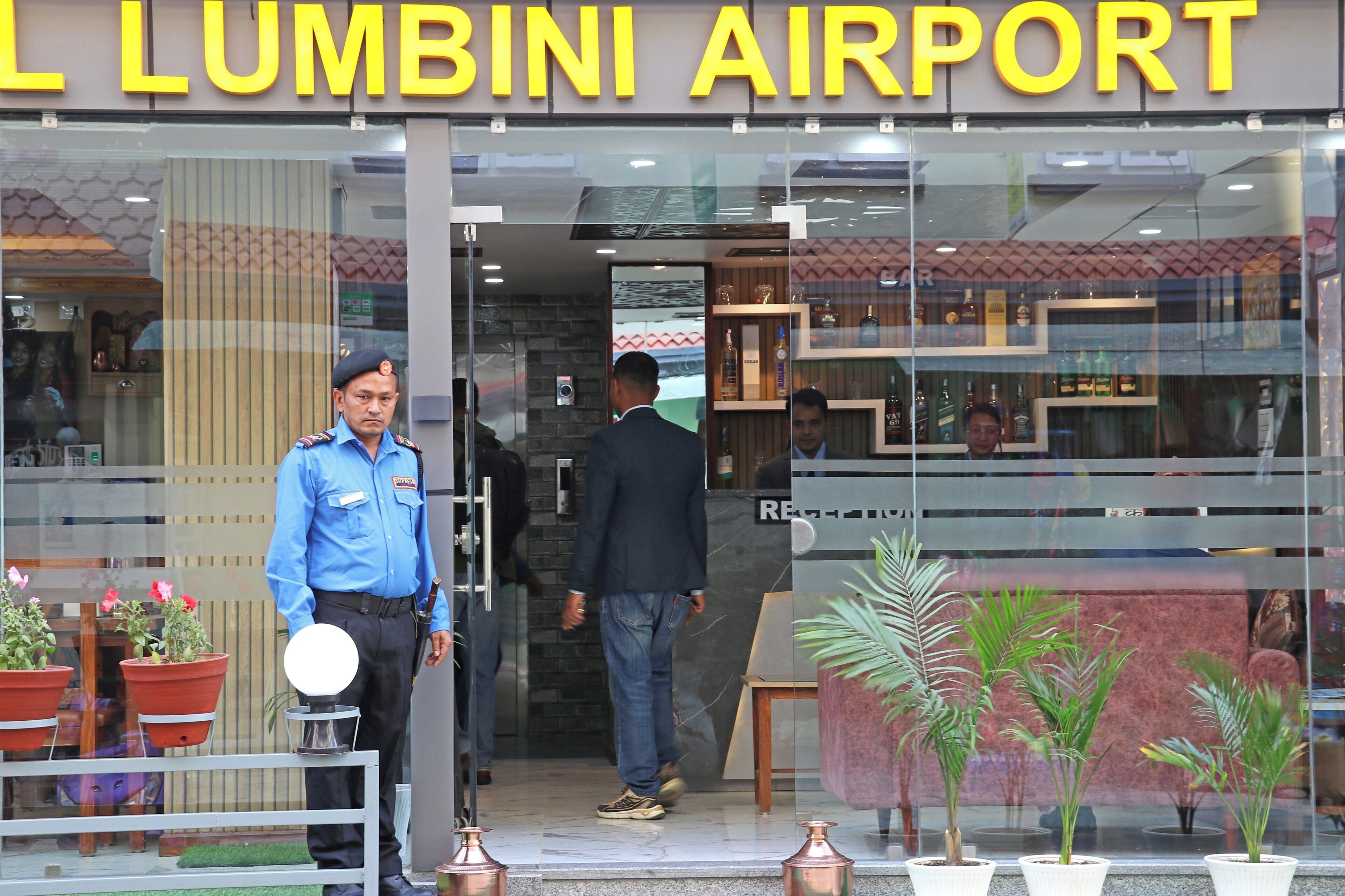 The entrance of Lumbini Airport with a security guard, potted plants, and a visible interior.