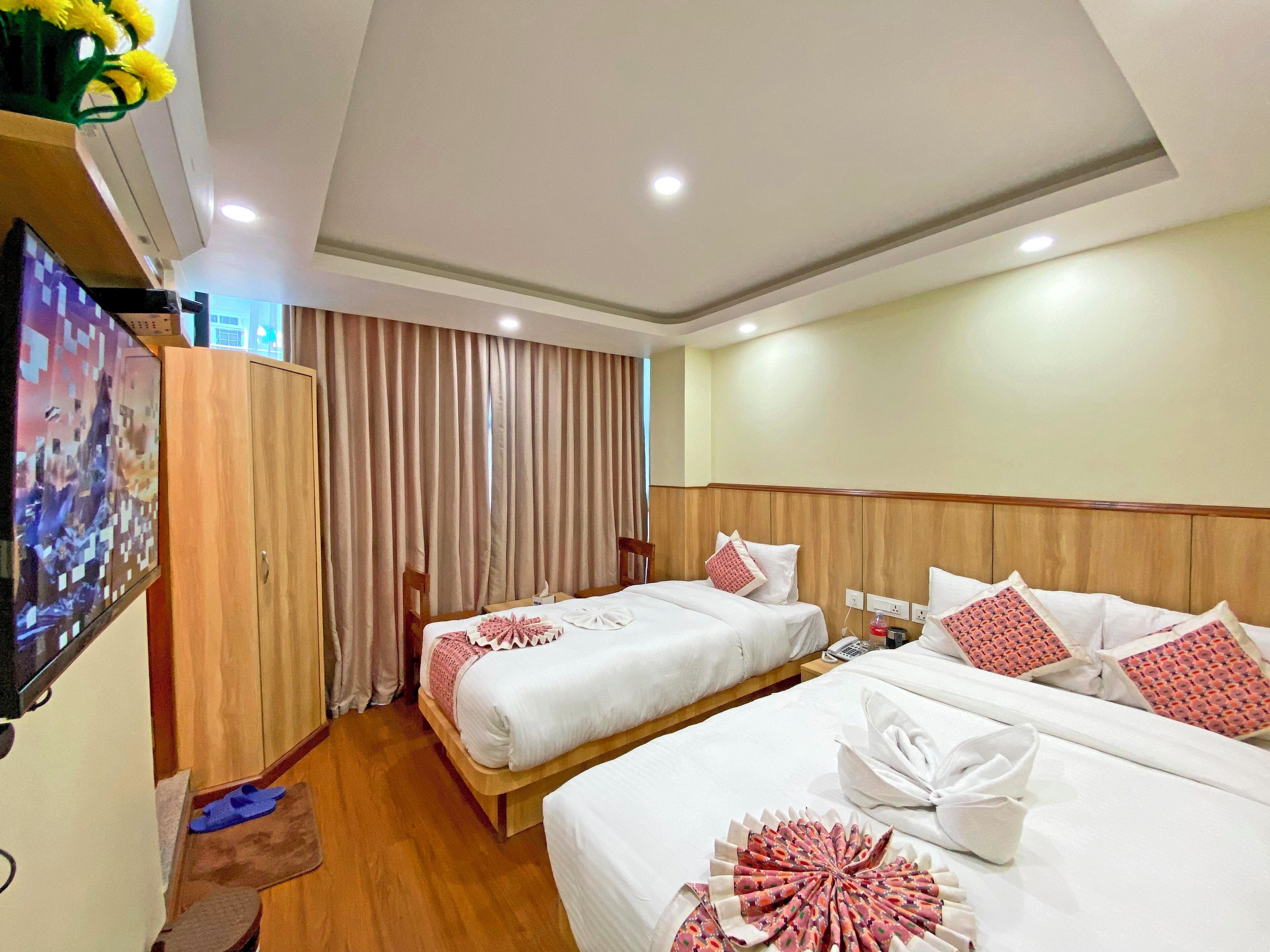 A hotel room with two beds, a TV, and a wooden wardrobe.