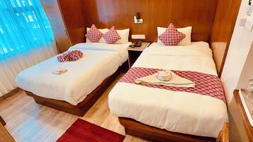 A hotel room with two beds, wooden headboards, a red rug, and a window with blue curtains.