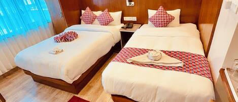Une chambre d’hôtel avec deux lits, des têtes de lit en bois, un tapis rouge et une fenêtre avec des rideaux bleus.