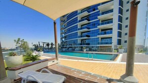 A modern building with a pool, a lounge area with a sunbed, and a clear view of the surrounding landscape. - WelHome - Relaxing and Fancy Studio Apt with City View (Dubai)