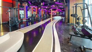 A gym with various exercise equipment, a central walkway, and a wooden accent wall. - WelHome - Relaxing and Fancy Studio Apt with City View (Dubai)