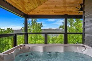 A hot tub with a wooden ceiling and large windows overlooking a green landscape.