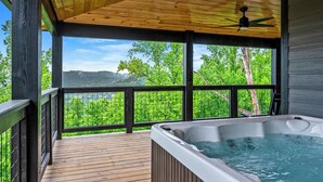 Un jacuzzi en una terraza de madera con vistas a árboles verdes y montañas.