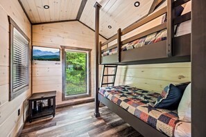 A cozy cabin with a bunk bed, wooden walls, a small table, and a window with a mountain view.