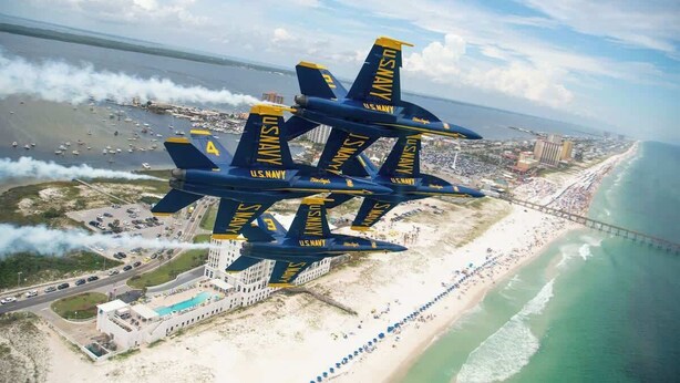 Un groupe d’avions de l’escadron de voltige de la marine américaine, les Blue Angels, survolent une zone côtière avec une plage et un pont.