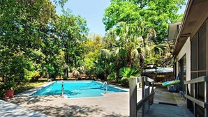 Une piscine entourée d’une végétation luxuriante, une terrasse en bois et un espace abrité avec des parasols.