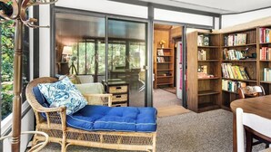 Un coin lecture confortable avec un fauteuil en osier, un coussin bleu et une bibliothèque remplie de livres.