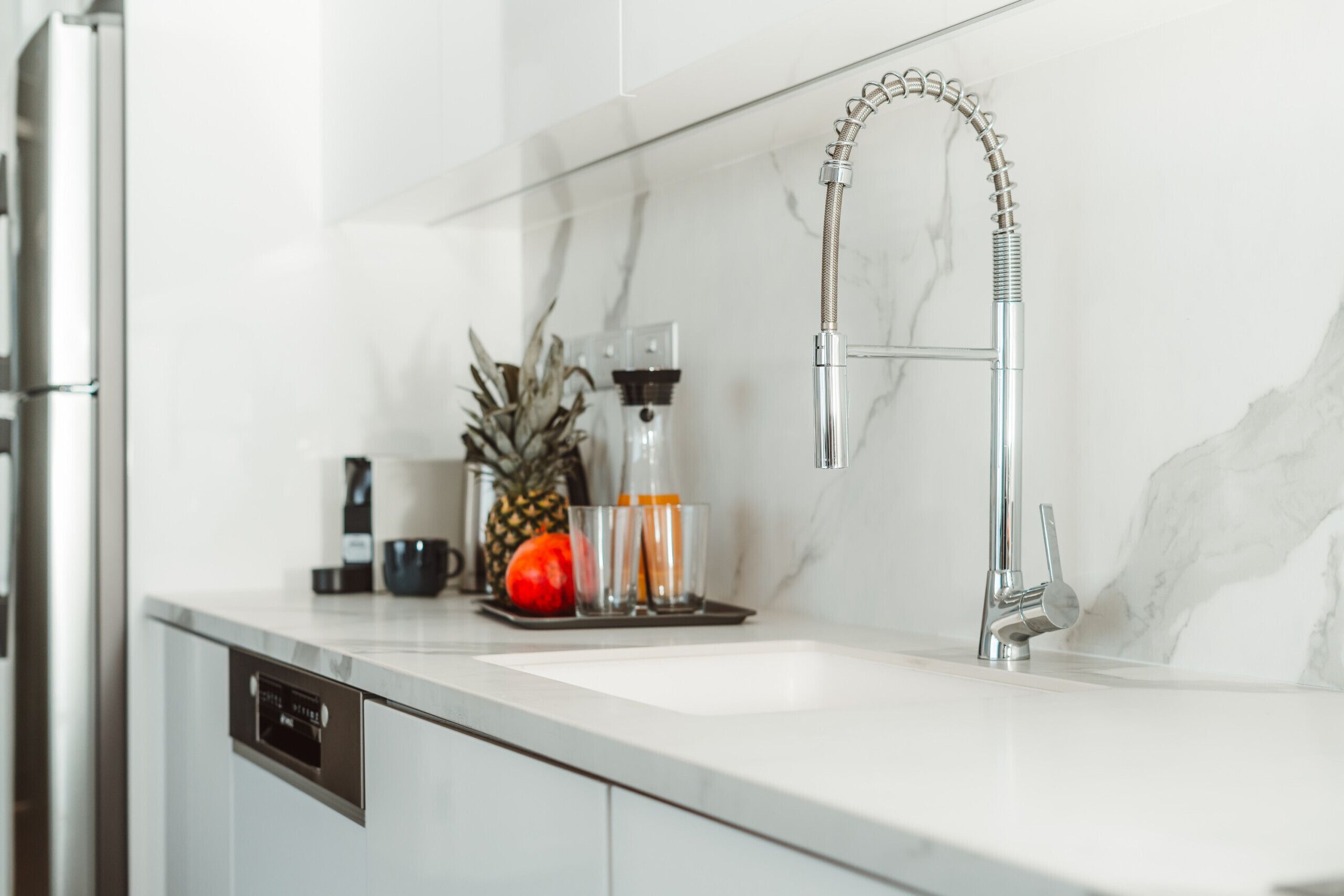 A modern kitchen with a stainless steel refrigerator, a built-in dishwasher, a white marble backsplash, and a sleek faucet.