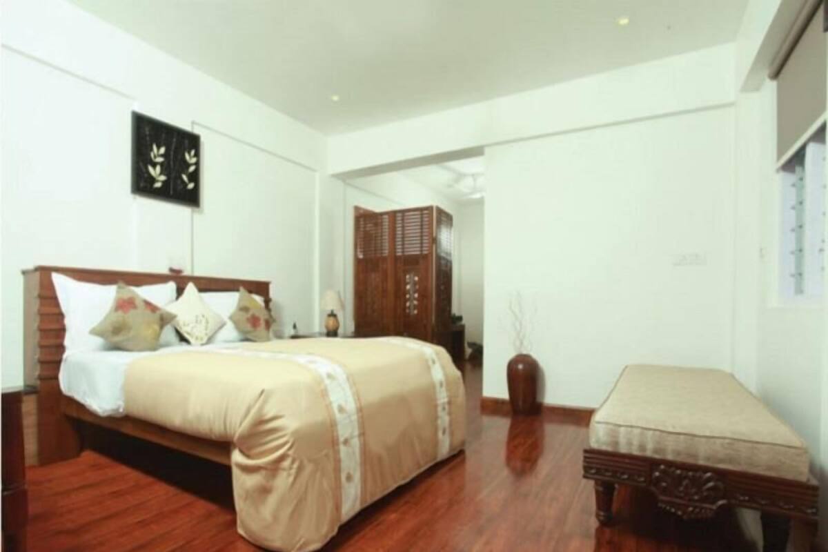 A bedroom with a wooden bed, a bedside table, a nightstand, a wardrobe, and a small sitting area.