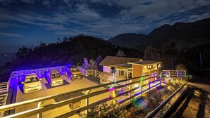 Un bâtiment moderne doté d’un toit plat et de panneaux solaires, entouré d’un parking bien éclairé et offrant une vue pittoresque sur les montagnes.