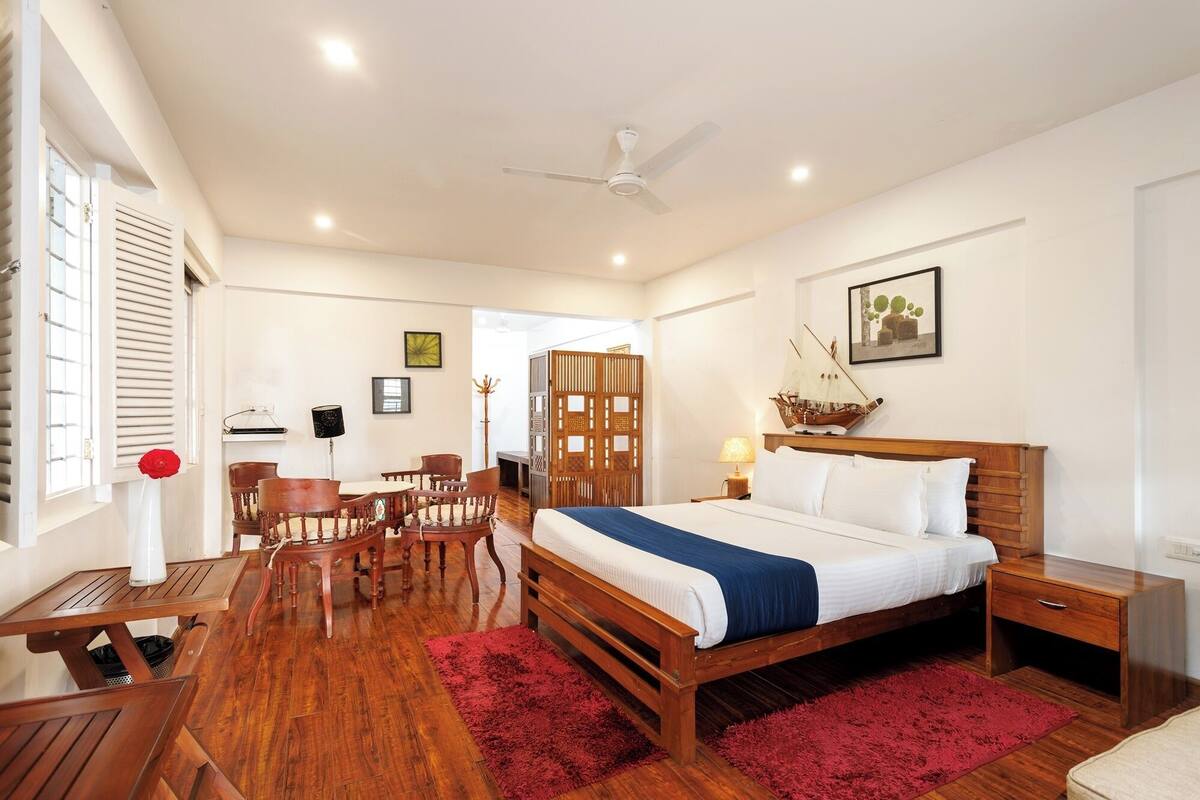 A hotel room with a wooden bed, a desk, a chair, a red rug, and a ceiling fan.