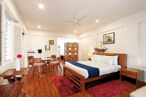 Ein Hotelzimmer mit einem hölzernen Bett, einem Schreibtisch, einem Stuhl, einem roten Teppich und einem Deckenventilator.